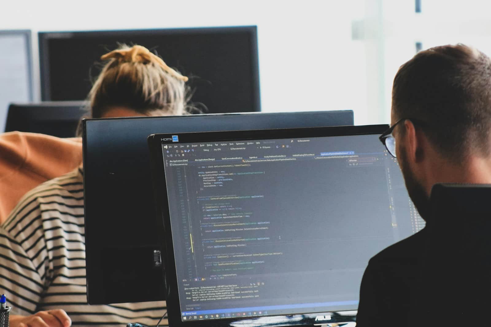 Two people writing code at their monitors in a bright office