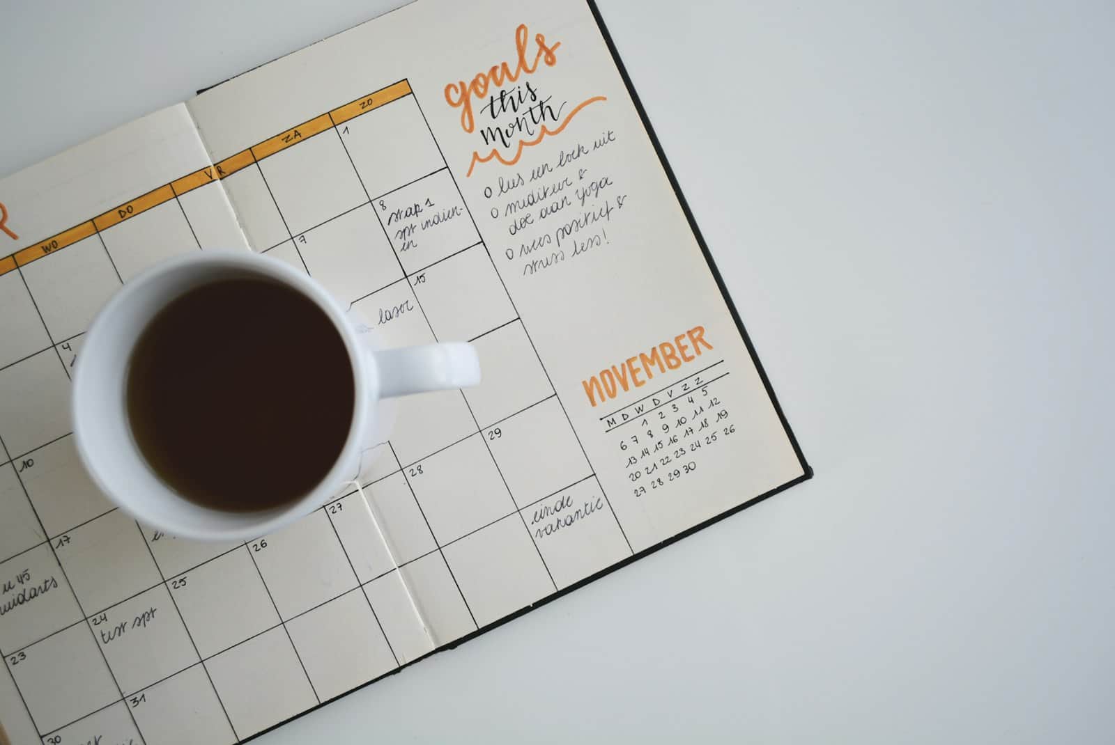 Open monthly planner with a calendar and a cup of coffee, seen from above