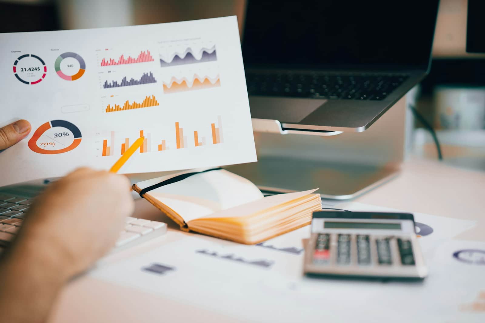 Hand pointing at a budget chart next to a laptop, notebook and calculator