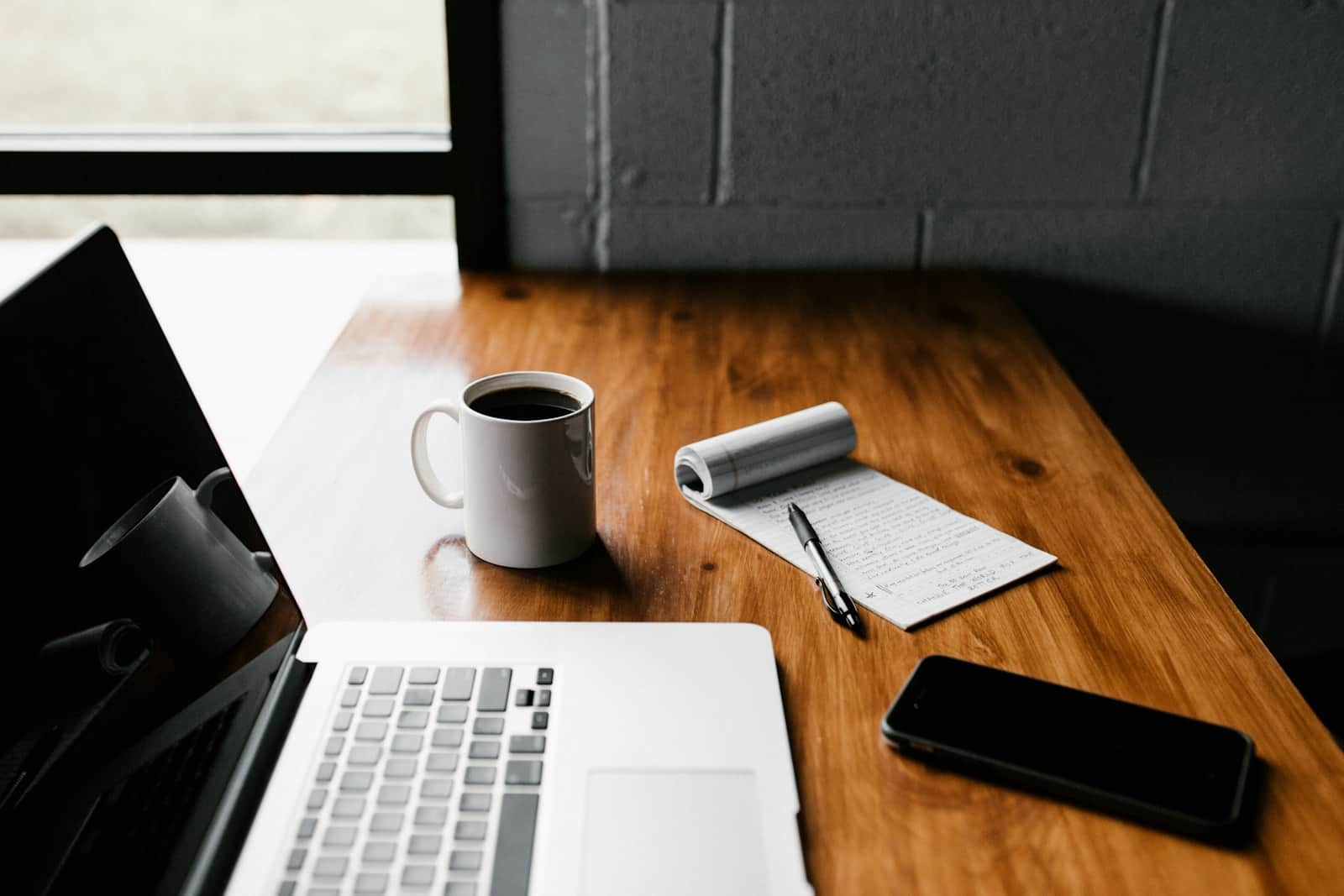 Tidy wooden desk with a laptop, coffee mug, notepad and phone