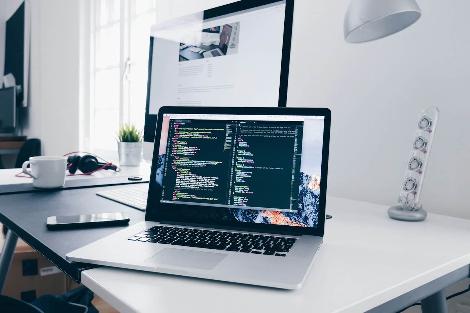 Laptop showing website code on its screen, on a white desk
